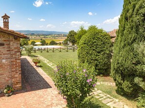 A brick building with a tower, a well-maintained lawn, and a view of distant fields. - Agriturismo il Querciolo (Marciano della Chiana)