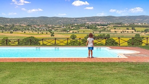 Ein Pool mit drei Markierungen für die Wassertiefe, umgeben von einer Rasenfläche und Blick auf eine Stadt sowie Hügel im Hintergrund.