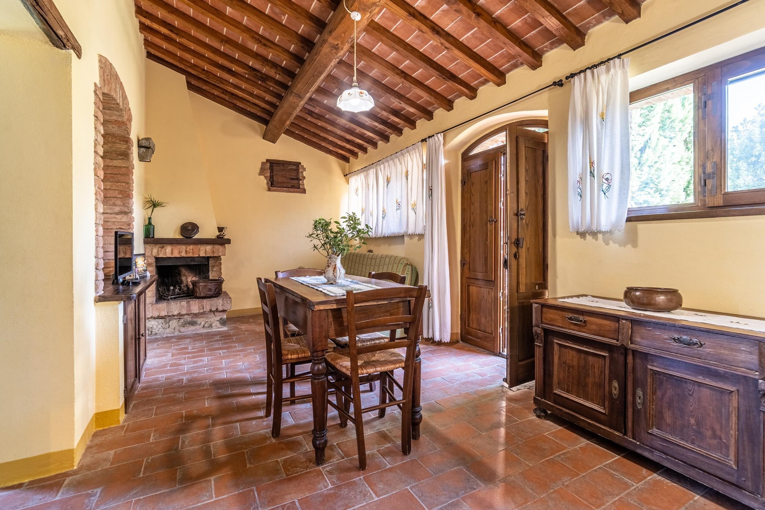 A rustic kitchen with a brick fireplace, wooden dining table, and cabinets.