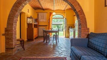 A cozy interior with a stone archway, a dining area with a table and chairs, and a sofa in a bright room with yellow walls.