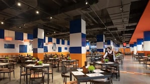 A spacious restaurant with multiple tables and chairs, a waiter in uniform, and a modern ceiling with exposed pipes. - Yinghai Hotel Apartment Zhuhai Chimelong (Zhuhai)
