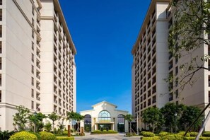 A modern hotel with a central entrance, surrounded by high-rise buildings, and a clear blue sky. - Yinghai Hotel Apartment Zhuhai Chimelong (Zhuhai)