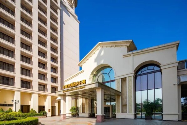 Ein Hotel mit einem großen, bogenförmigen Glas Eingangsbereich, heller Fassade und einem mehrstöckigen Gebäude mit Balkonen.