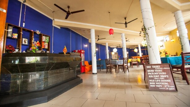 A hotel lobby with a reception desk, multiple dining areas, and a sign listing available tours. - Sana's Beach Guesthouse and Restaurant (Negombo)