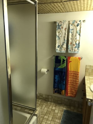 A bathroom with a shower, a toilet, and a sink. There are two towels hanging on the wall, one with a nautical theme and another with a floral pattern.