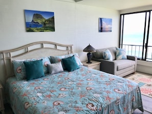 A bedroom with a bed, a nightstand, a sofa, and a view of the ocean.