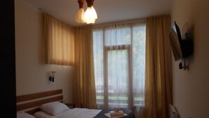 Ein Hotelzimmer mit zwei Betten, einem an der Wand befestigten Fernseher und einem großen Fenster mit Vorhängen.