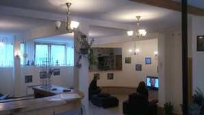 Ein Wohnzimmer mit Couchtisch aus Holz, einer schwarzen Couch und einem Fernseher. Zwei Kronleuchter, ein Fenster mit Vorhängen und ein Kamin aus Stein sind ebenfalls vorhanden.