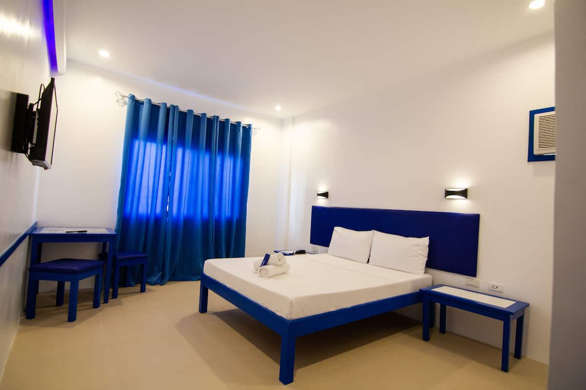 A modern hotel room with a bed, bedside tables, a desk, and chairs.