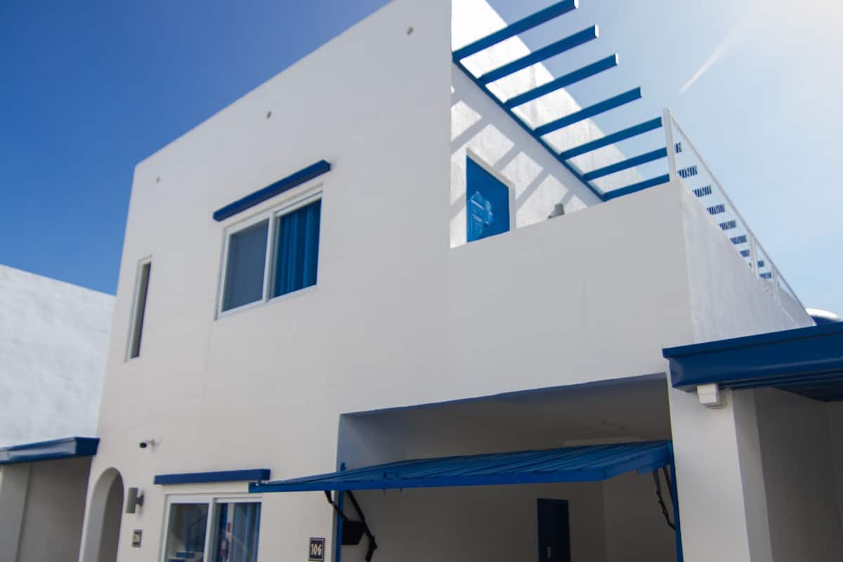 A modern two-story building with a blue staircase, a fire extinguisher, and a small plant by the entrance.