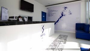 A hotel reception area with a white reception desk, a mounted flat-screen TV, a blue couch, and a wall map listing attractions. - Skytel Palawan (Puerto Princesa)