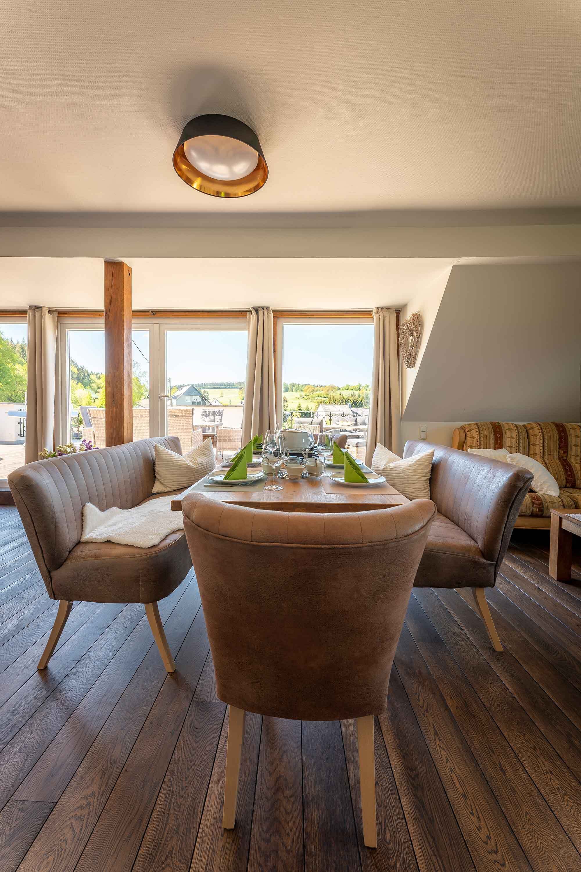 Ein modernes Wohnzimmer mit einem runden Tisch, zwei Ledersofas und großen Fenstern mit Blick ins Freie.