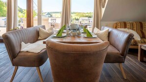 A modern living room with a round table, two leather sofas, and large windows offering a view of the outdoors. - Old forest house in the Eifel (Ormont)