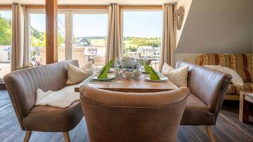 Ein modernes Wohnzimmer mit einem runden Tisch, zwei Ledersofas und großen Fenstern mit Blick ins Freie.
