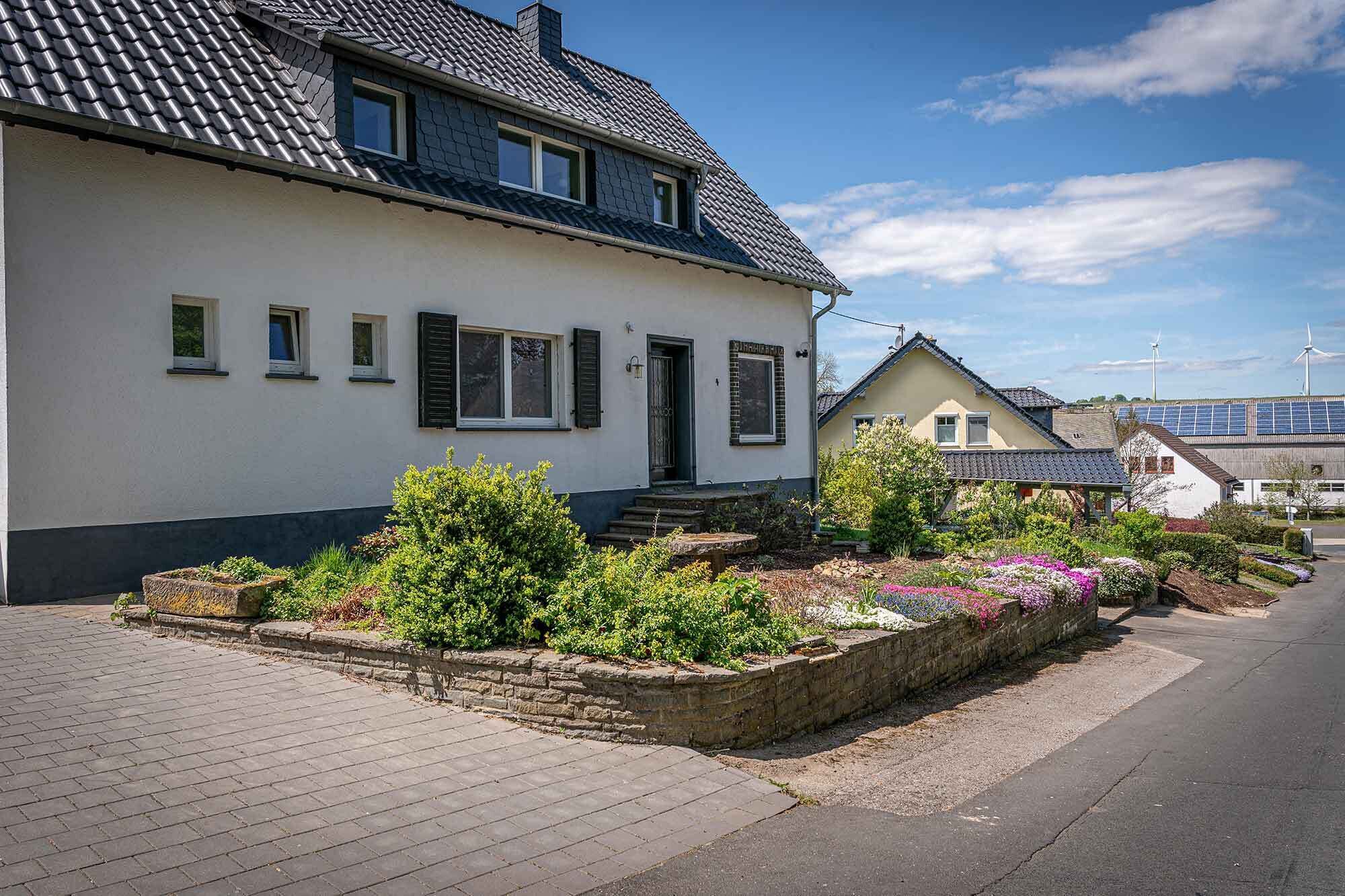Ein zweistöckiges Haus mit Garten, einer gepflasterten Auffahrt und einem Windrad im Hintergrund.