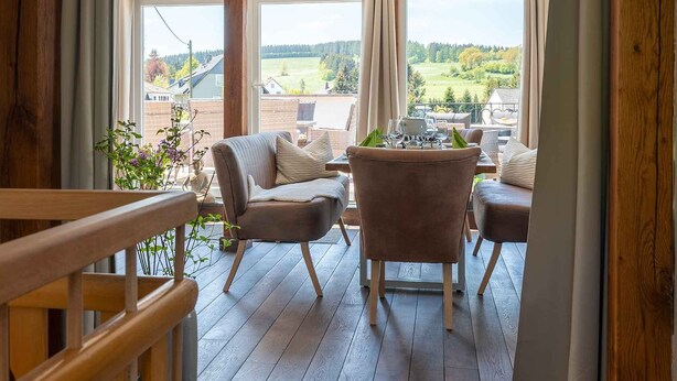 A spacious room with a wooden floor, a dining table with chairs, and a view of a green landscape through large windows. - Old forest house in the Eifel (Ormont)