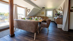 A dining area with a wooden table set for four, a sofa, and a view of the outdoors. - Old forest house in the Eifel (Ormont)