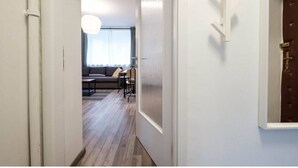 Un couloir mène à un espace de vie comprenant un canapé, des fauteuils et un luminaire suspendu.