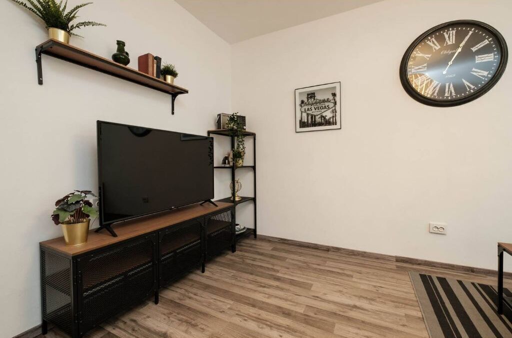 Un salon doté d’un téléviseur à écran plat, d’un parquet, d’une grande horloge murale et d’un tableau encadré.