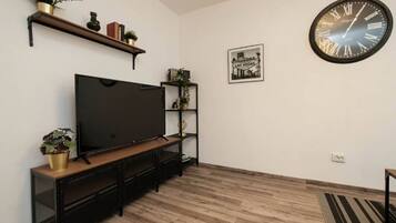 Un salon doté d’un téléviseur à écran plat, d’un parquet, d’une grande horloge murale et d’un tableau encadré.