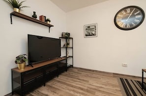 Ein Wohnzimmer mit Flachbildfernseher, Holzboden, einer großen Wanduhr und einem gerahmten Bild.