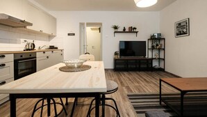 Une cuisine moderne avec des meubles blancs, une table à manger en bois et un téléviseur dans l’espace salon.