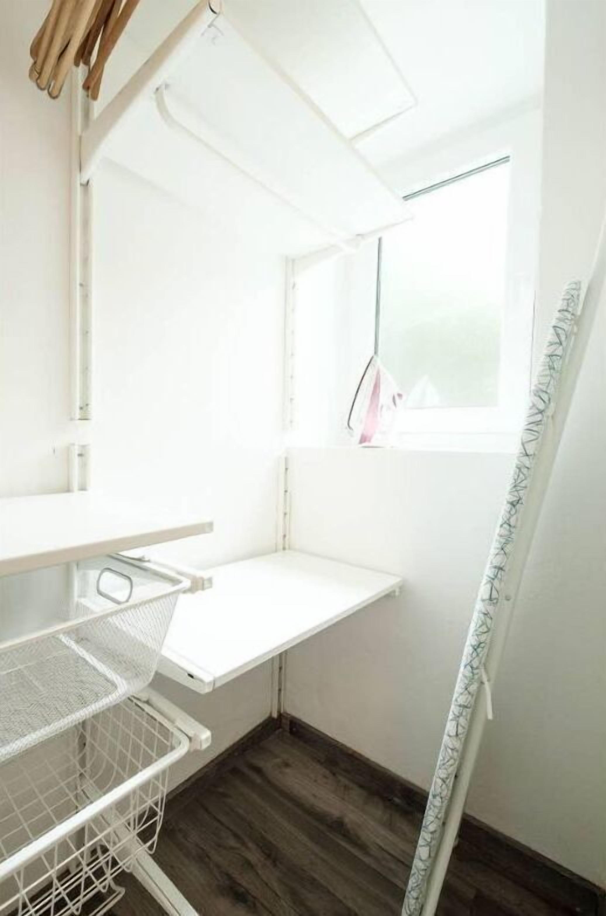 Eine Raumecke mit weißer Decke, einem Fenster mit Ausblick und einem weißen Regal mit Korb.