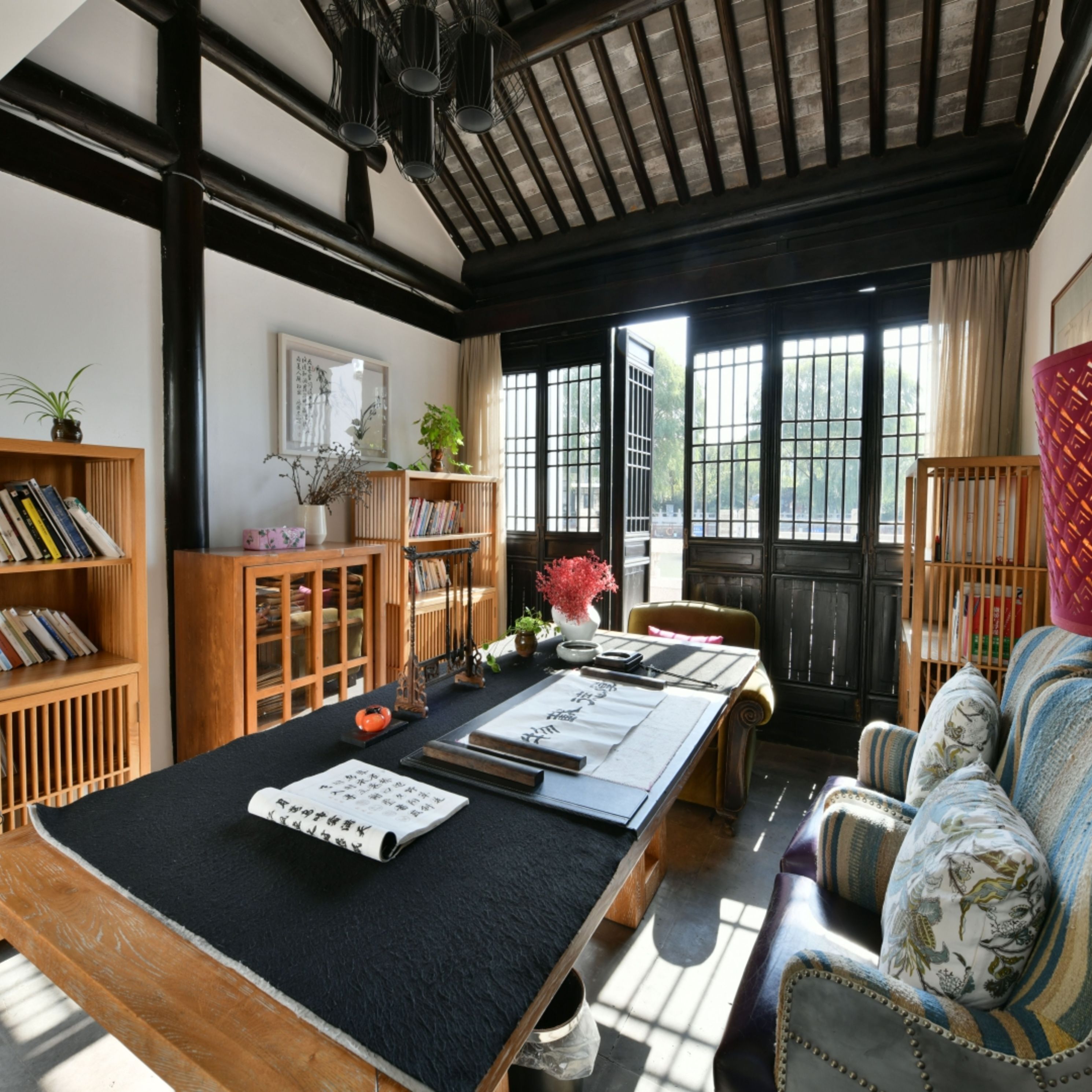 A traditional Japanese-style room with tatami flooring, a low table with calligraphy, a sofa with patterned cushions, and a view through large shoji doors.