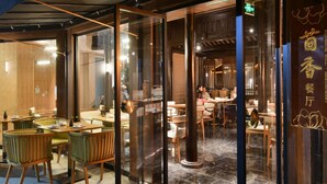 Un intérieur moderne avec des portes vitrées donnant sur un espace repas agrémenté de meubles en bois et d’une enseigne de restaurant bien visible.
