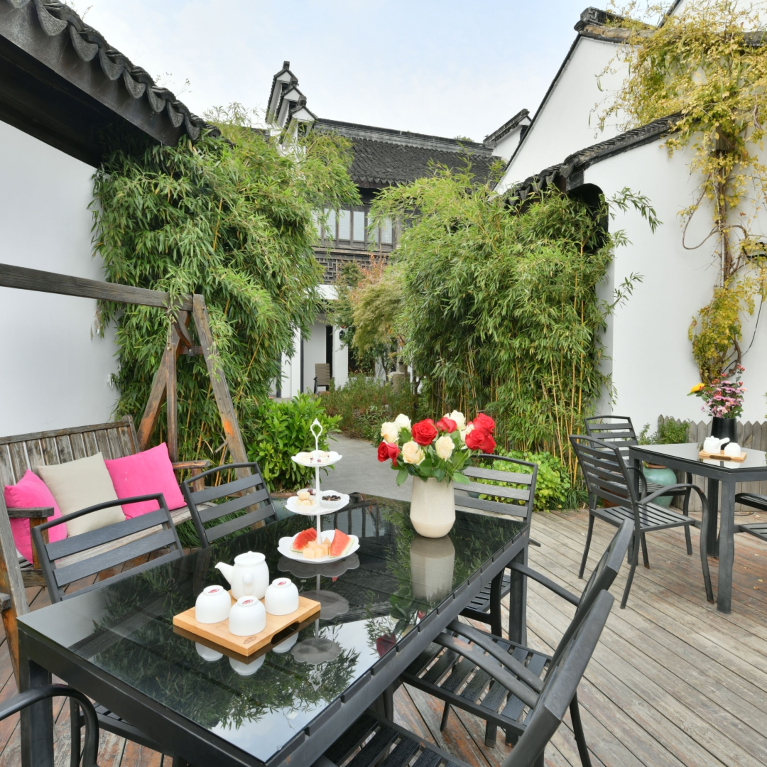 A glass-top table with chairs, a bench with cushions, and a small outdoor dining area with a table set for tea.
