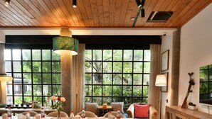 Un vaste espace dédié à la salle à manger, avec une longue table en bois, de nombreuses chaises et une vue sur la verdure grâce à de grandes fenêtres.