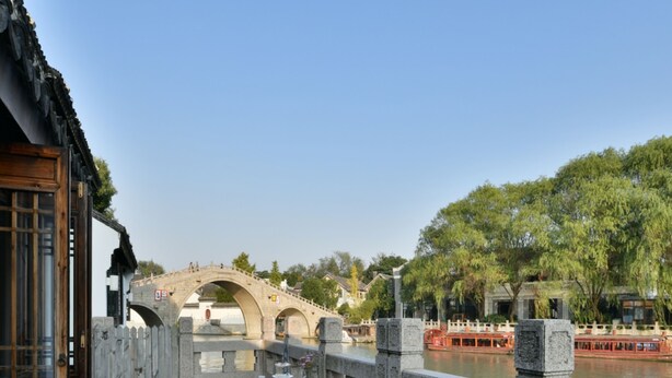 Une terrasse avec des tables dressées pour le dîner, offrant une vue sur une rivière et un pont de pierre.