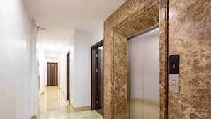 A hallway with a marble floor, a wooden door, and an elevator with a marble wall. - Victoria Hotel Ninh Binh (Hoa Lu)