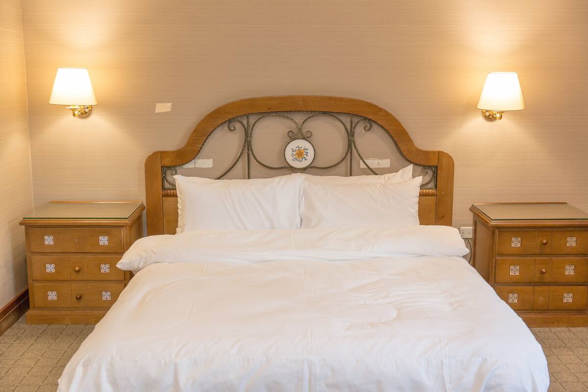 A neatly made bed with white linens, two bedside tables with drawers, and wall-mounted lamps.