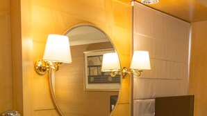 Une chambre d’hôtel compacte comprenant un bureau en bois, deux lampes fixées au mur, un téléviseur à écran plat, un petit réfrigérateur et un miroir.