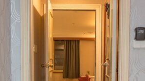 Un couloir d'hôtel avec des revêtements de sol en moquette, des portes ouvertes donnant sur une chambre avec un lit et une fenêtre avec des rideaux.