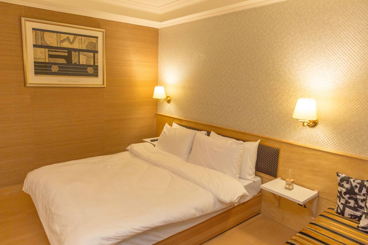 A hotel room with a large bed, two bedside tables, a headboard, and a framed picture on the wall.