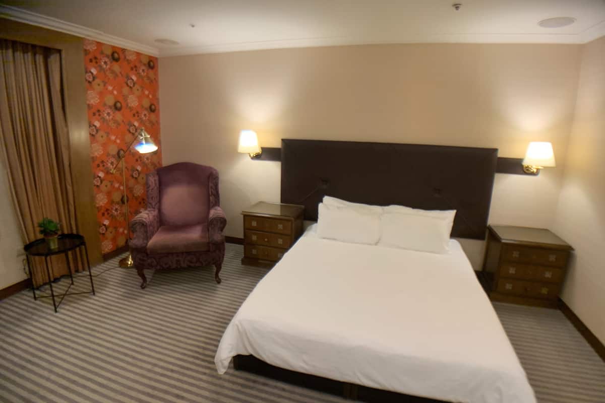A hotel room with a large bed, two nightstands, a chair, and a lamp.