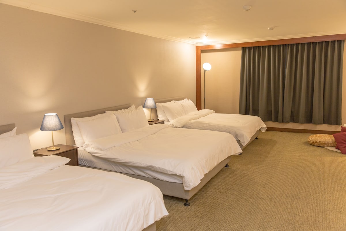A hotel room with two beds, a lamp, a curtain, and a carpeted floor.