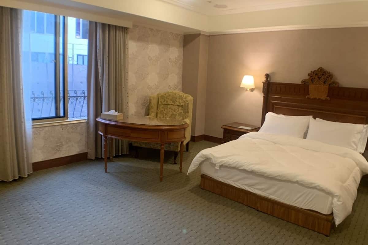 A hotel room with a bed, a chair, a table, and a nightstand.