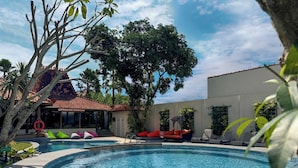 Una piscina amb gandules, una zona d'estar coberta i un edifici amb teulada de rajola.