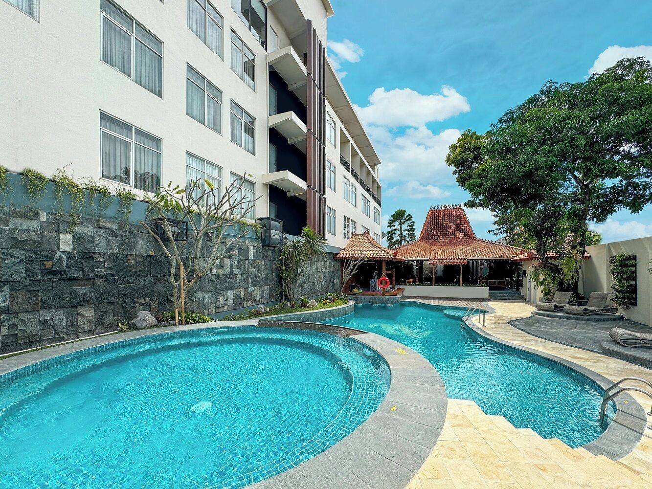A hotel with a swimming pool area, a covered outdoor seating area, and a building with multiple balconies.