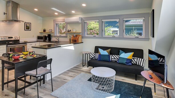 A modern kitchen with a dining area, a sofa with colorful cushions, and a TV on a stand. - Hawthorne Urban Loft Private ADU with Parking & AC (Portland)