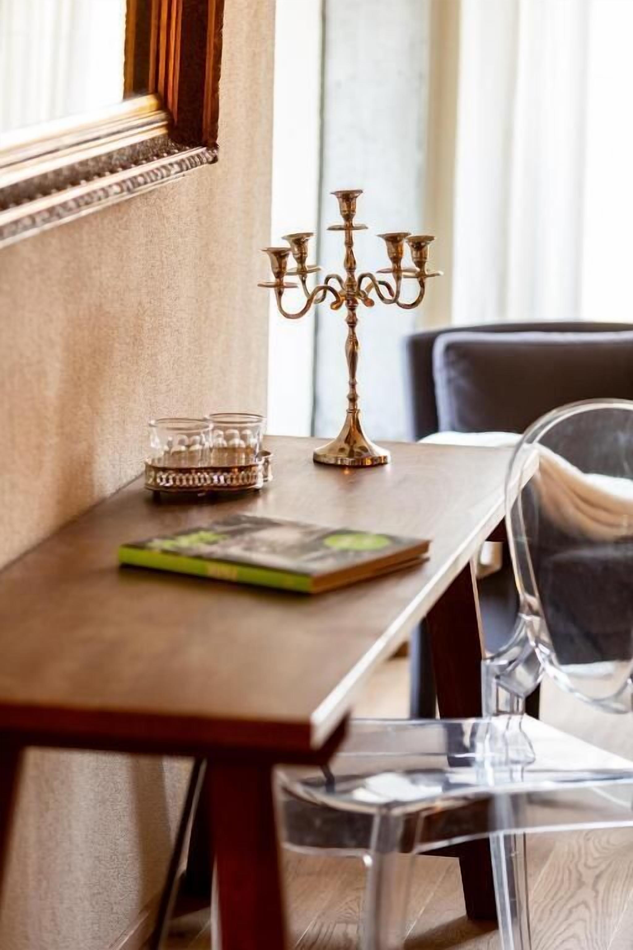 Une table en bois, sur laquelle se trouvent un chandelier en laiton, un porte-bougie en verre et un livre.
