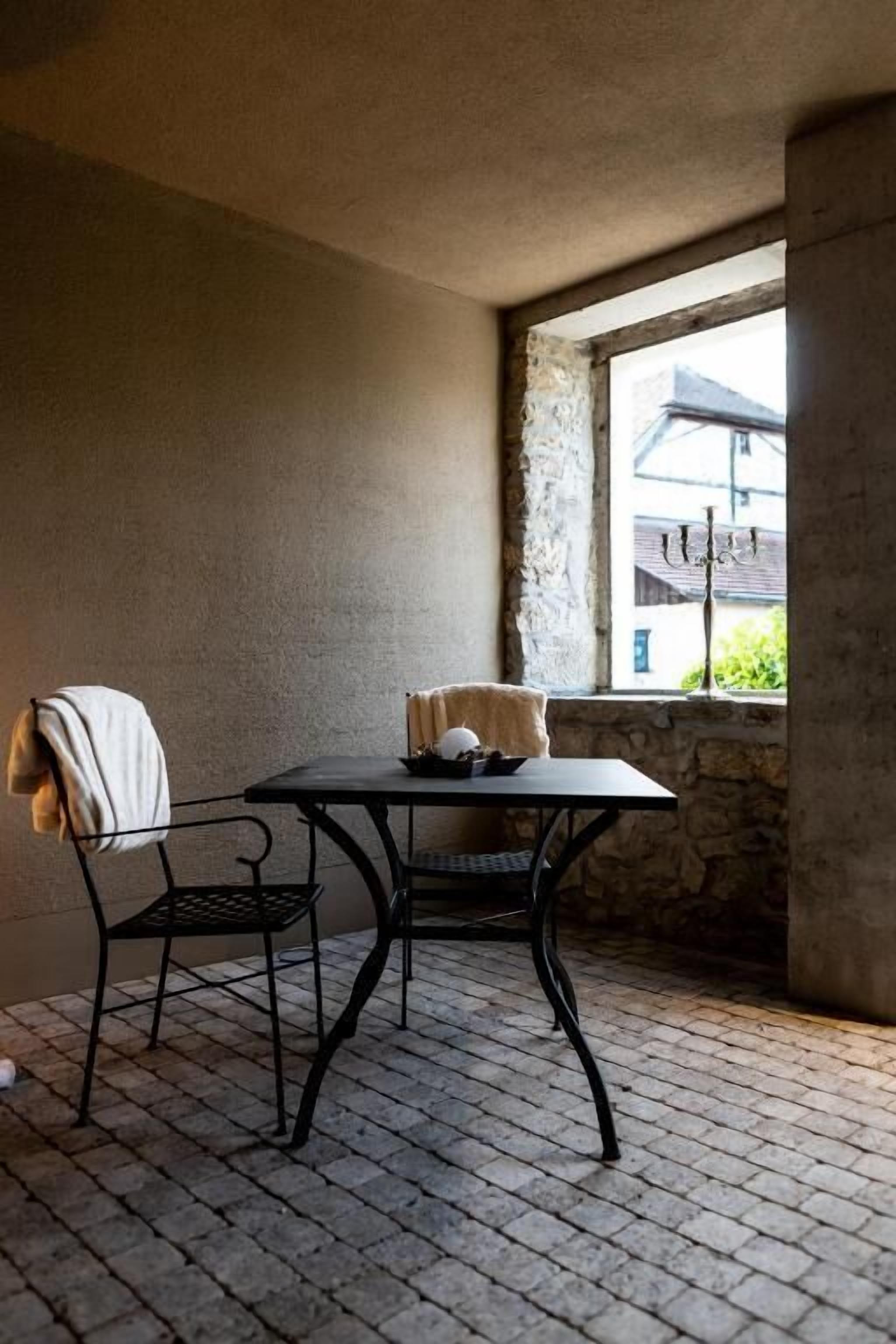 Quarto nos fundos com parede de pedra, janela com vista para edifícios, mesa com cadeira e radiador.