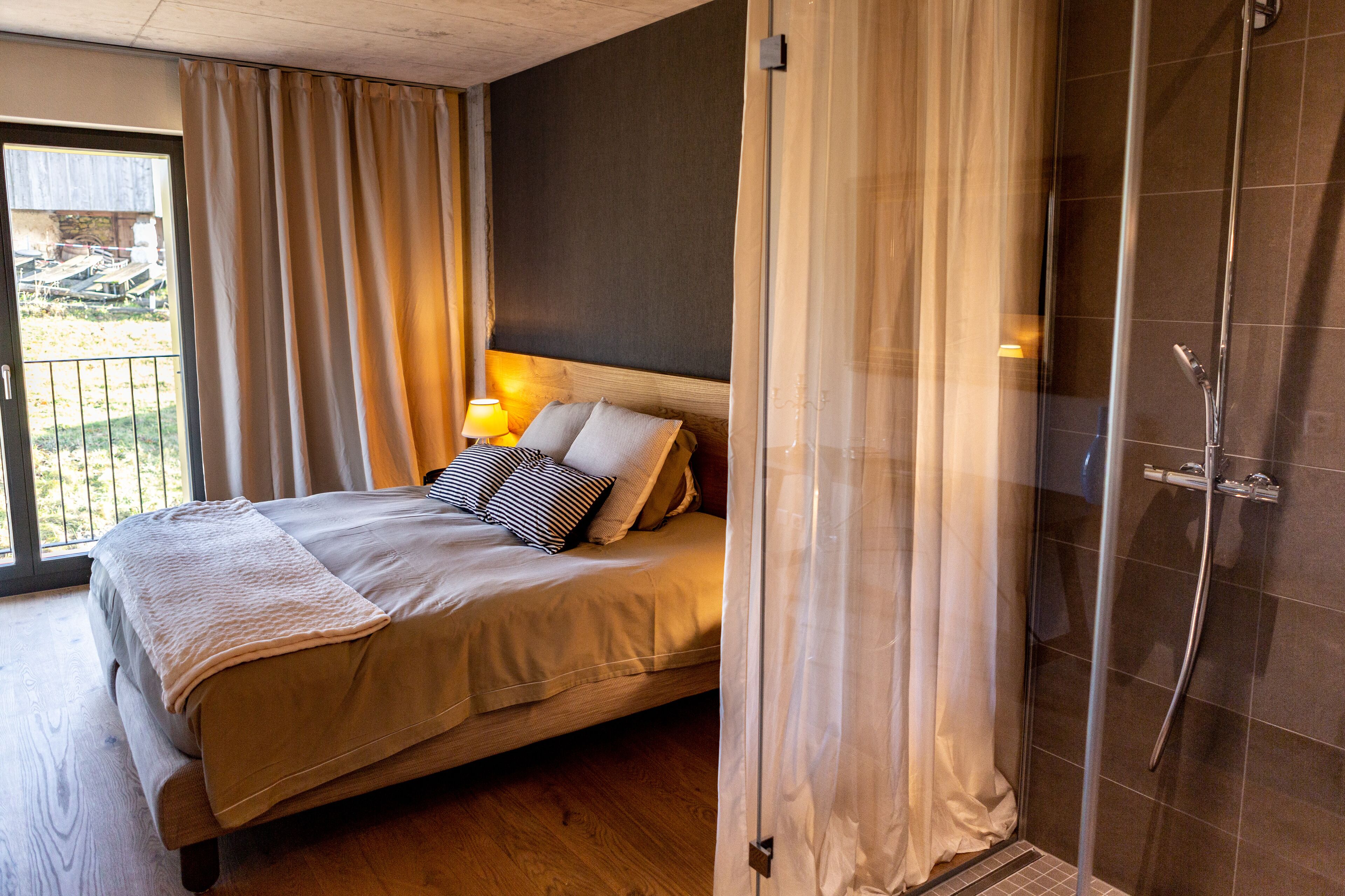 Ein Schlafzimmer mit Bett, Vorhängen, einem Nachttisch und einer Dusche.