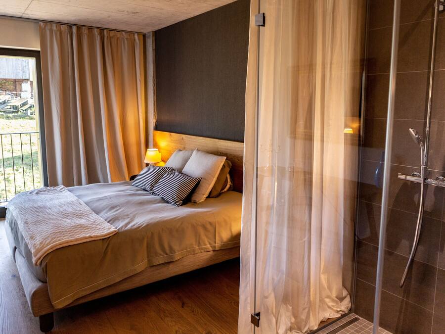 Un dormitorio con cama, cortinas, mesita de noche y zona de ducha.