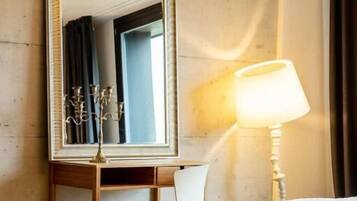 Una habitación de hotel con un espejo grande, una lámpara de noche, una cama y suelo de madera.