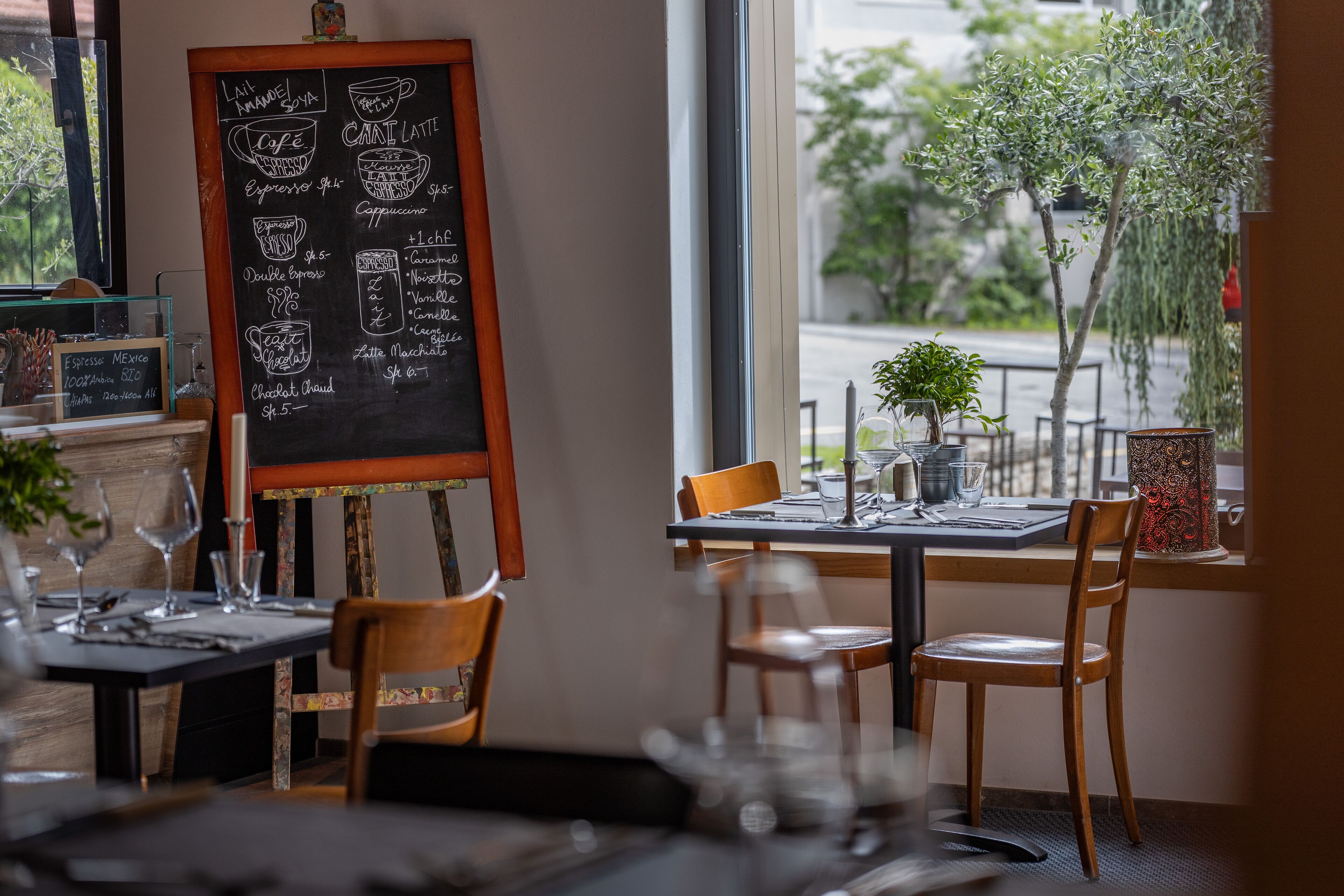 Interior de restaurante con un menú en pizarra, sillas de madera y vistas a la calle.
