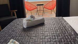 Habitación de hotel con cama, dos sillas, una mesita y vista al mar.